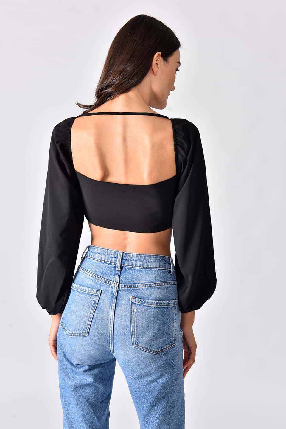 Model wearing trendy crop top in black color, in pose from behind