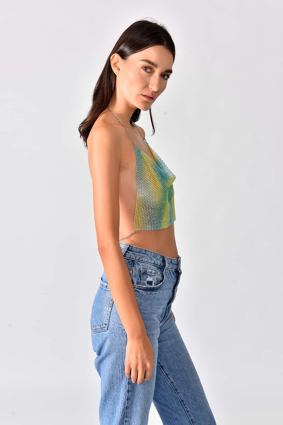 Model wearing shiny crop top in green-yellow gradient color, posing from the left side