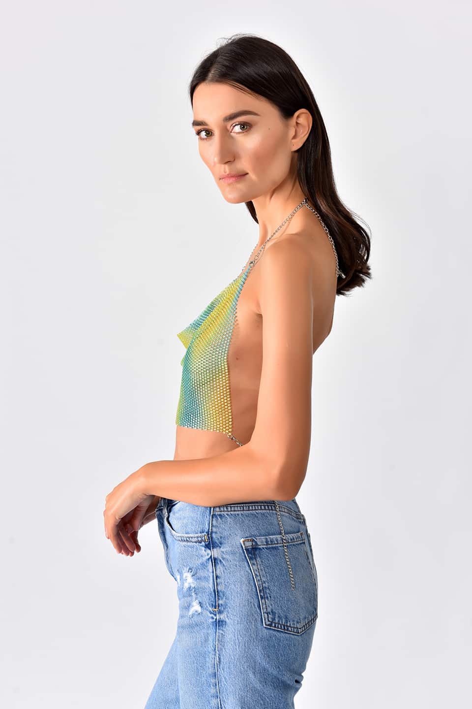 Model wearing shiny crop top in green-yellow gradient color, posing from the right side