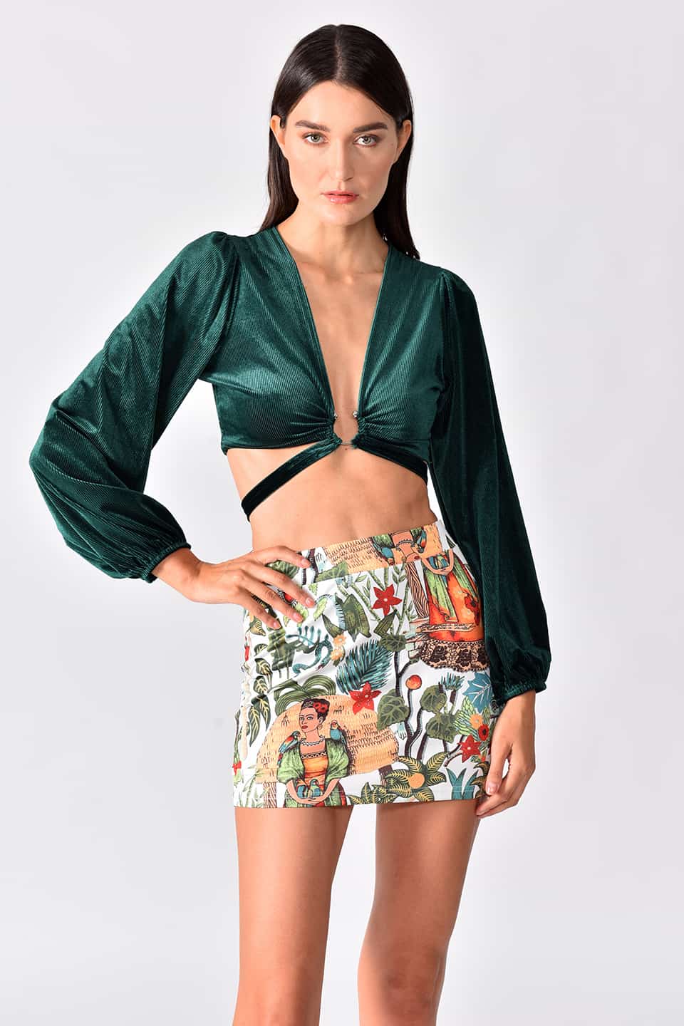Model in pose for front view, while wearing a set of colorful mini skirt and emerald green top with long sleeves.