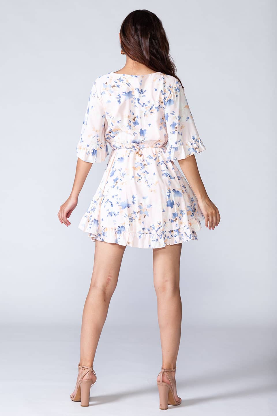 Whitish floral ruffled summer mini dress with V-neck and short sleeves. Model posing for behind view