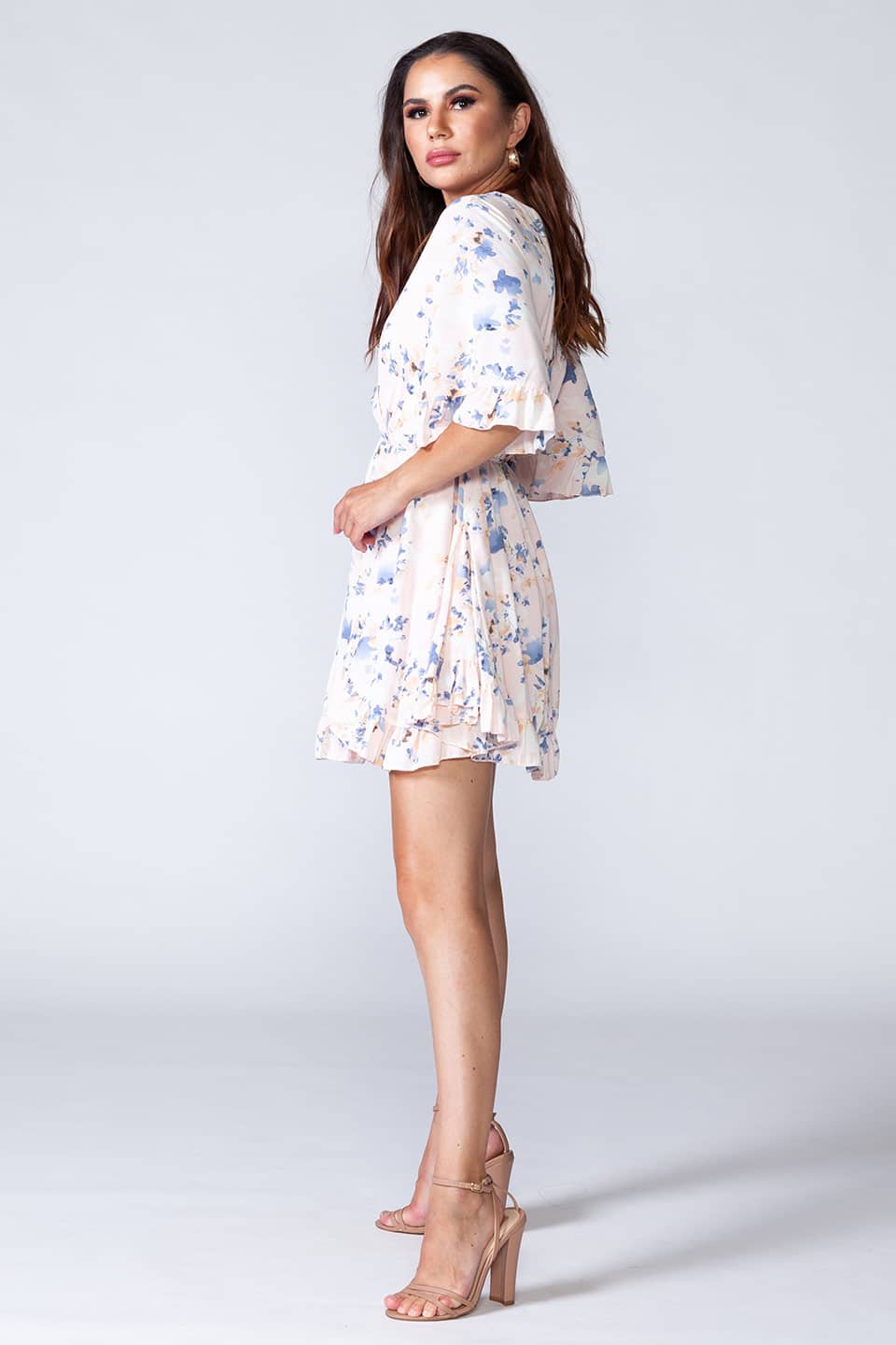 Whitish floral ruffled summer mini dress with V-neck and short sleeves. Model posing for side view