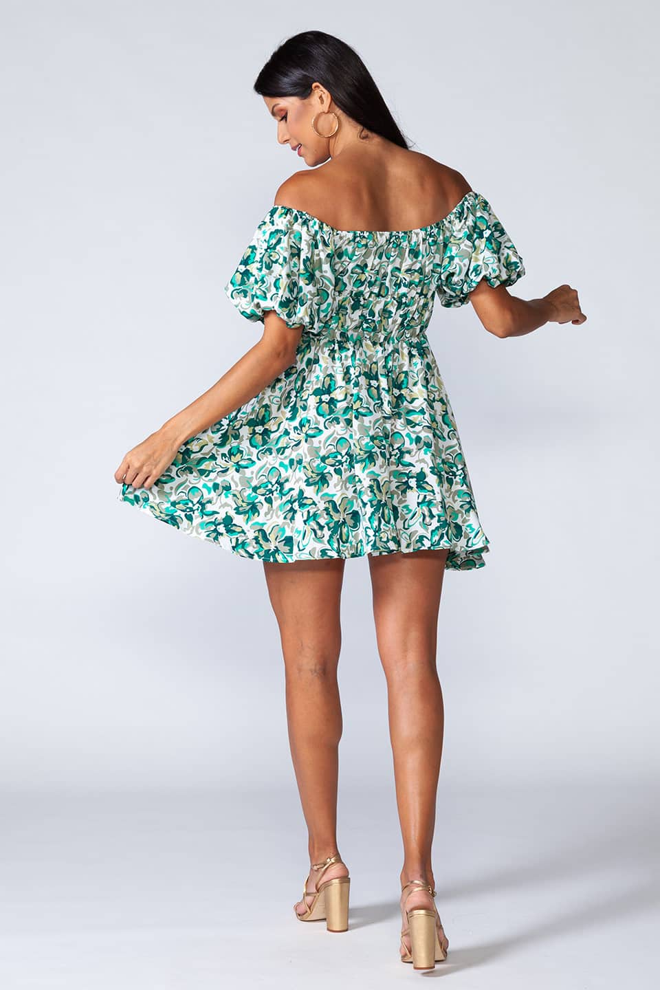 Off-shoulder mini dress with elastic waist and ruffled bottom of the skirt. Model posing for full body, behind view