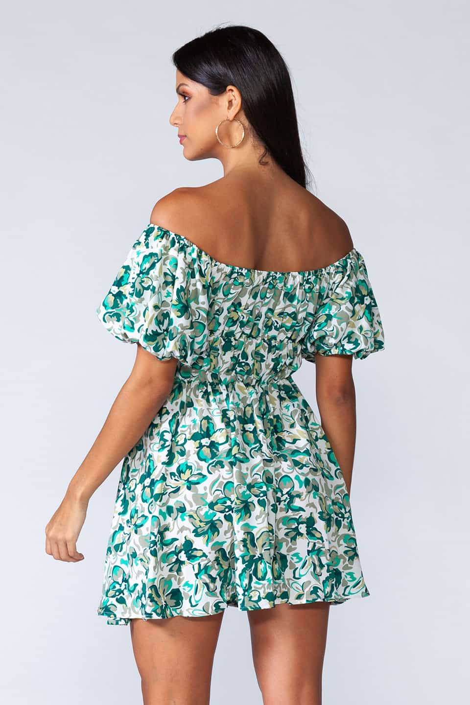 Off-shoulder mini dress with elastic waist and ruffled bottom of the skirt. Model posing from behind