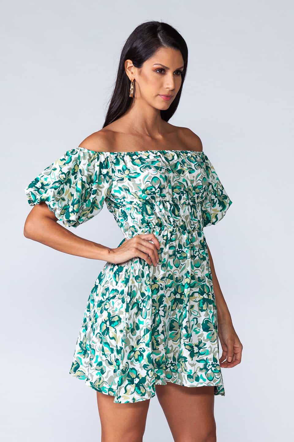 Off-shoulder mini dress with elastic waist and ruffled bottom of the skirt. Model posinf in front-side view