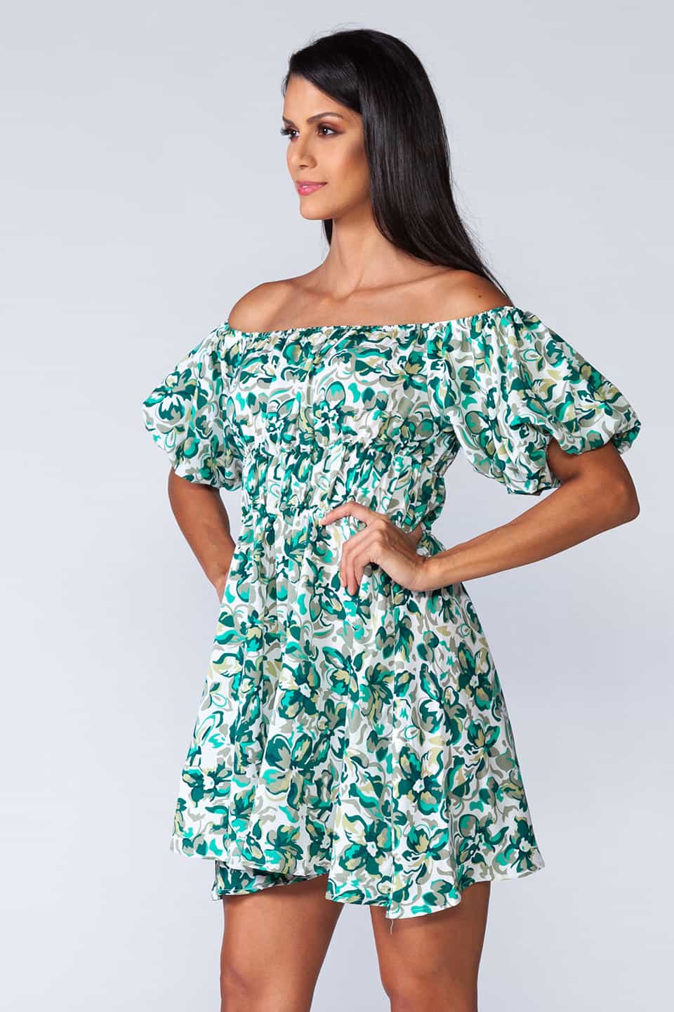 Off-shoulder mini dress with elastic waist and ruffled bottom of the skirt. Model side view
