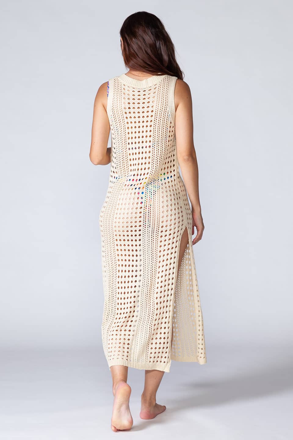 Hollowed-out kaftan in beige color, sleeveless and stretchable. Model posing for backside