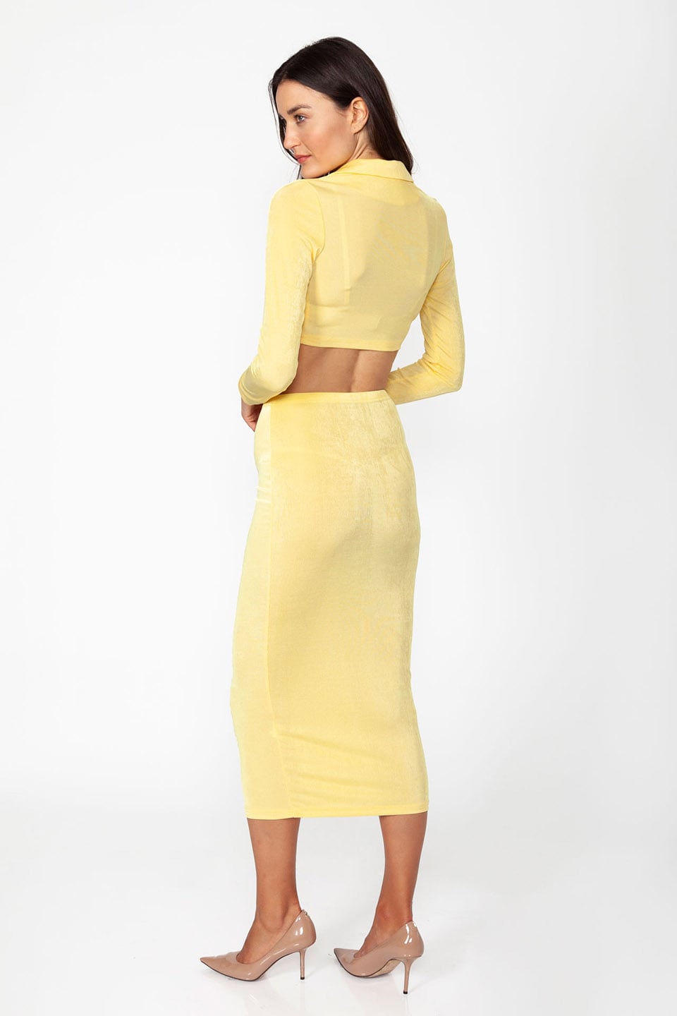 Model wearing set of top and skirt in yellow color with long sleeves and crop top posing from behind