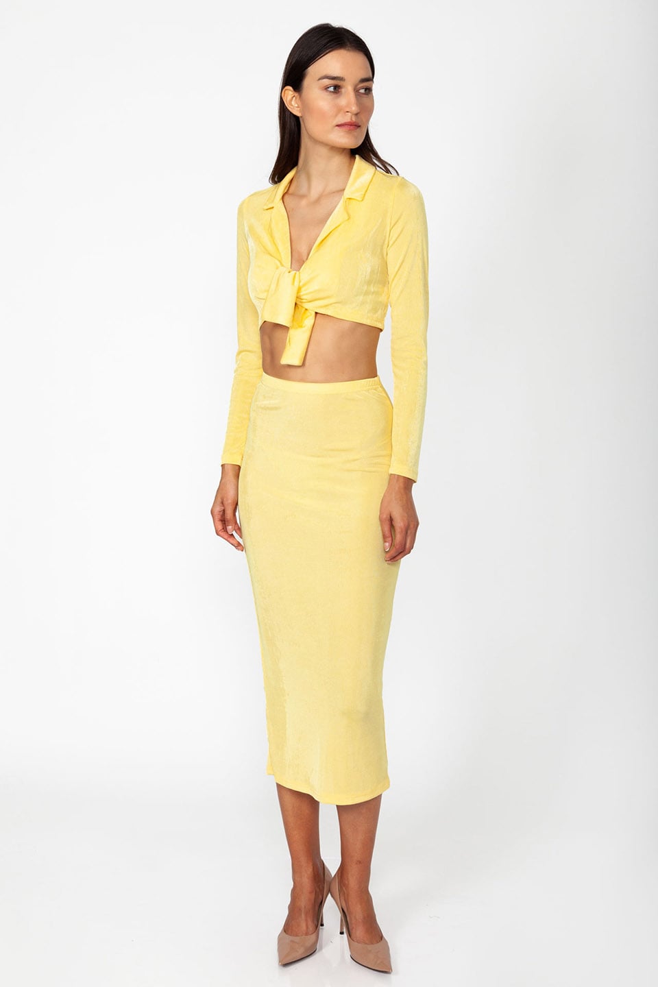 Model wearing set of top and skirt in yellow color with long sleeves and crop top.