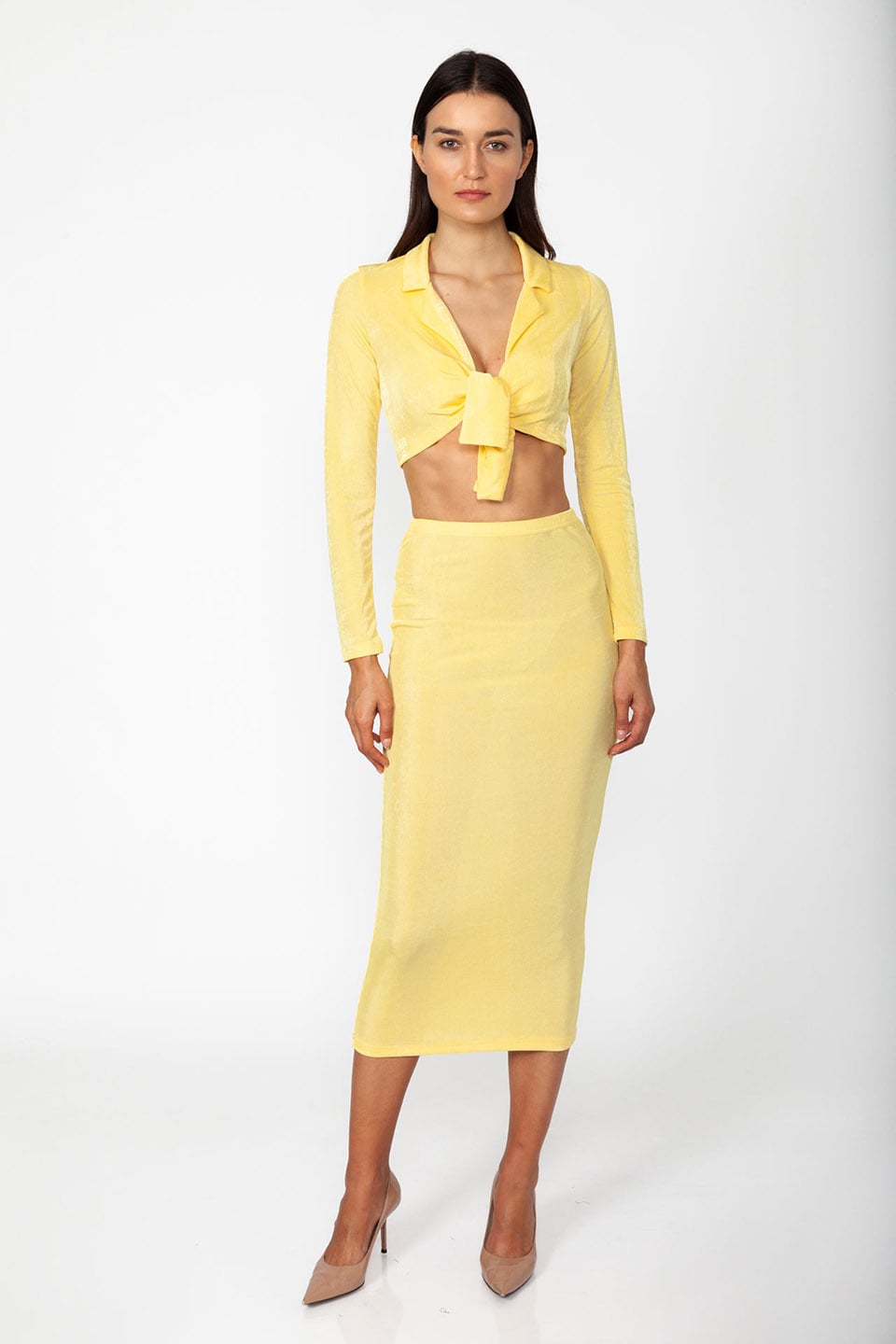 Model wearing set of top and skirt in yellow color with long sleeves and crop top, posing for front view
