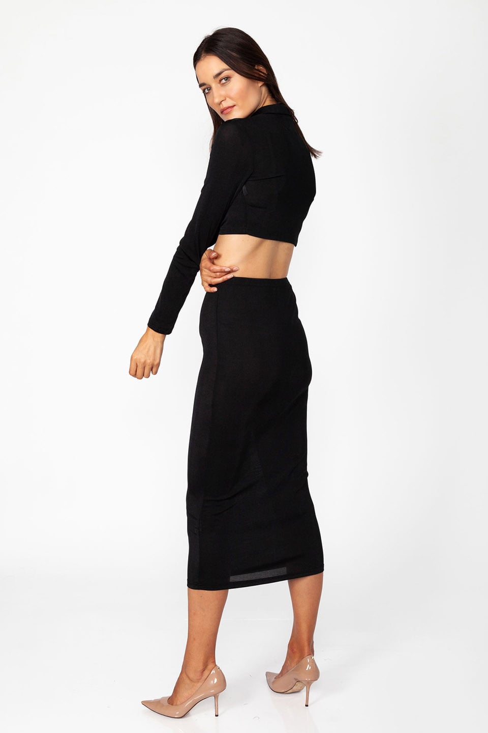 Model wearing set of top and skirt in black color with long sleeves and crop top, posing from behind