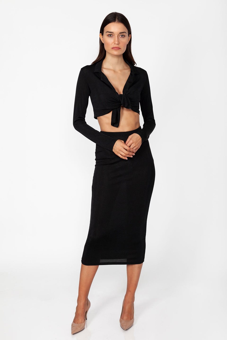 Model wearing set of top and skirt in black color with long sleeves and crop top, posing for front view