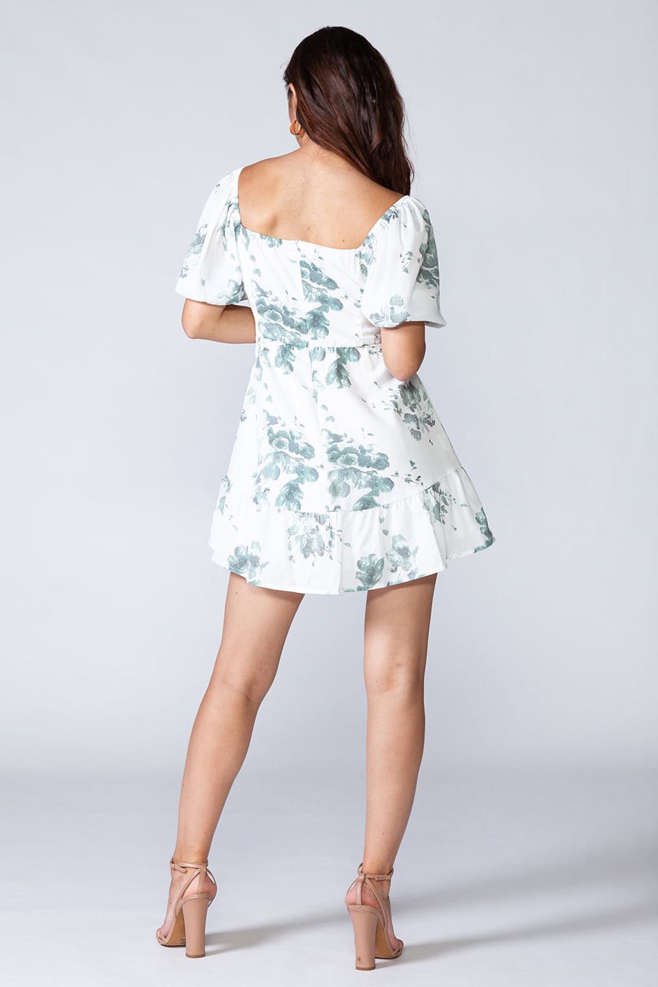 White mini dress with floral print, puff sleeves and cut-out front. Model posing from behind
