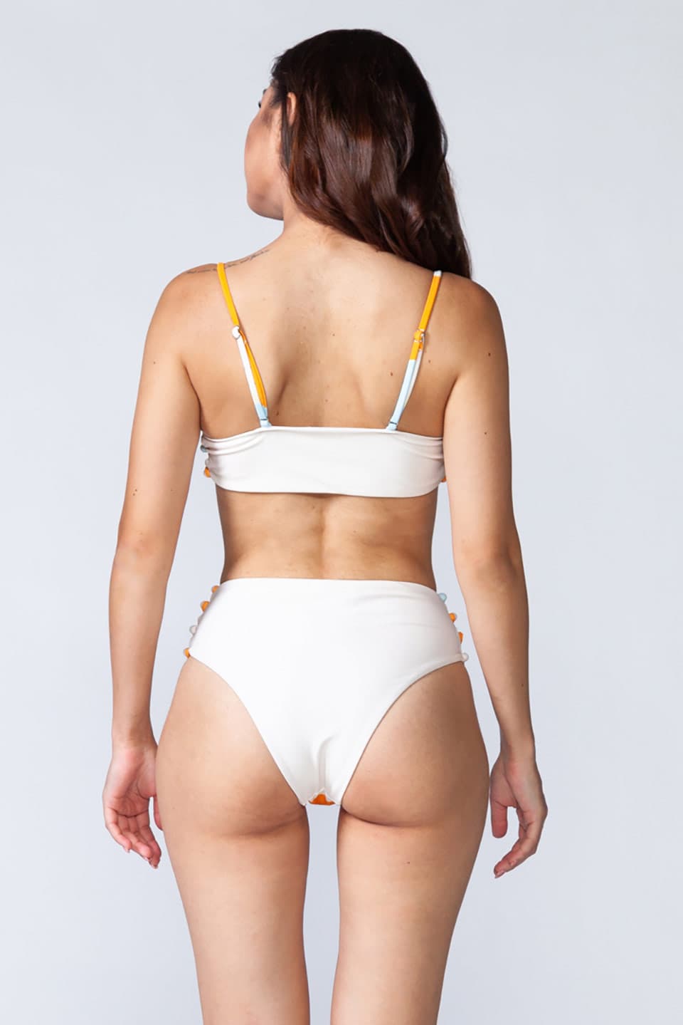 Model wears two-piece high waist bottom swimsuit, with adjustable straps and pearl look like buttons on the sides. Posing for behind view