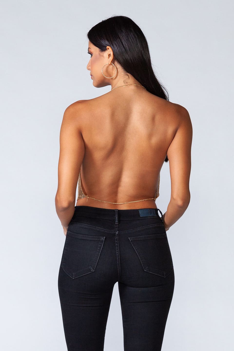 Model wears metal crop top in gold color, posing for behind view