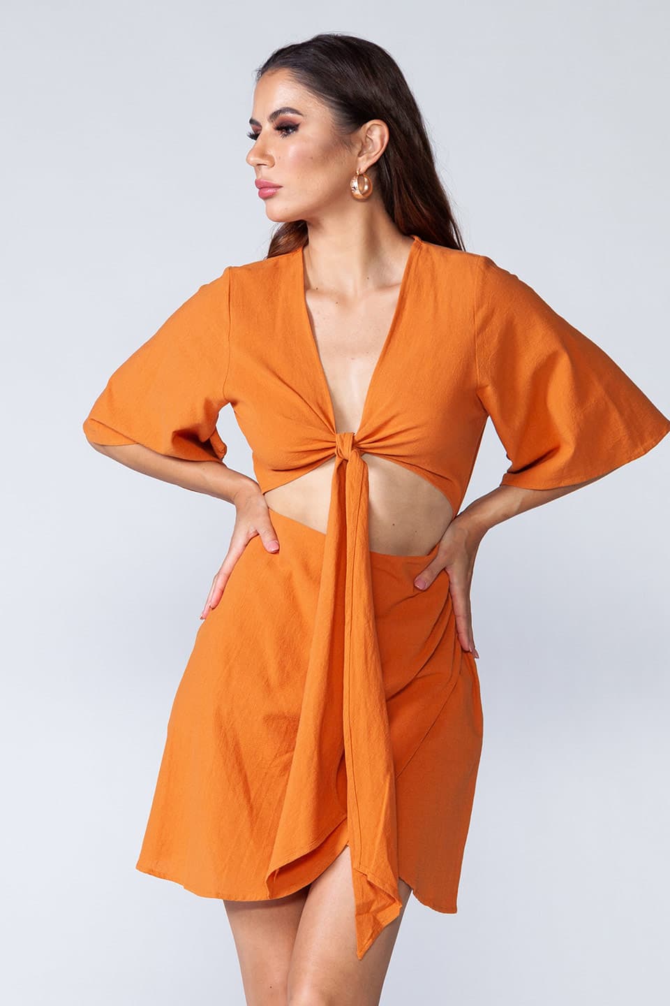 Model wearing cotton mini dress with open cut-out front that ties in knot, in pose looking aside