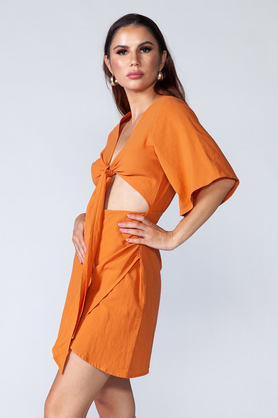 Model wearing cotton mini dress with open cut-out front that ties in knot, in a side pose